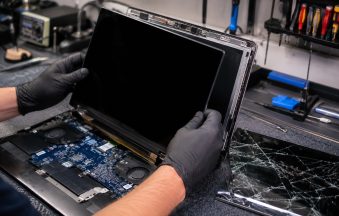 CompuMaster technician wearing protective gloves installing a new laptop screen while replacing a cracked display in a professional computer repair workshop.