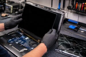 CompuMaster technician wearing protective gloves installing a new laptop screen while replacing a cracked display in a professional computer repair workshop.