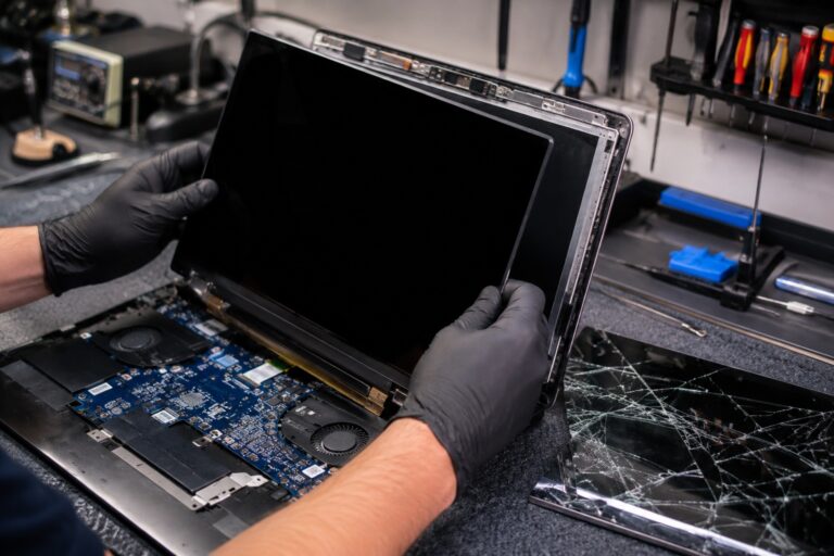 CompuMaster technician wearing protective gloves installing a new laptop screen while replacing a cracked display in a professional computer repair workshop.